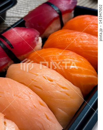 Black container with variety of fresh orange and red sushi pieces Black container with variety of fresh orange and red sushi pieces 141947002