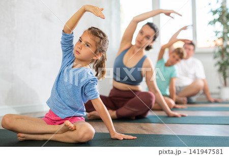 Mother and family performing yoga exercises at yoga studio, family health concept Mother and family performing yoga exercises at yoga studio, family health concept 141947581