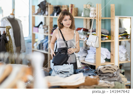 Positive young girl choosing handbag in clothing store Positive young girl choosing handbag in clothing store 141947642