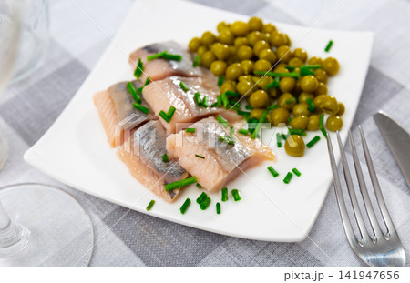 Pieces of herring served with green peas and onions. Appetizer fish on table Pieces of herring served with green peas and onions. Appetizer fish on table 141947656