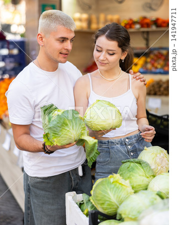 Married couple near vegetable stand in store choose cabbage Married couple near vegetable stand in store choose cabbage 141947711