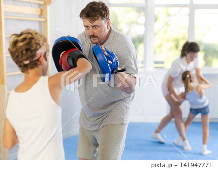 Boy and dad are boxing in gym, father helps child to work out force of blow. Boy and dad are boxing in gym, father helps child to work out force of blow. 141947771