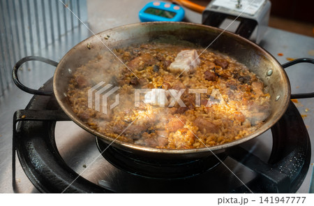 Spanish paella with meats and mushrooms simmering in pan 141947777