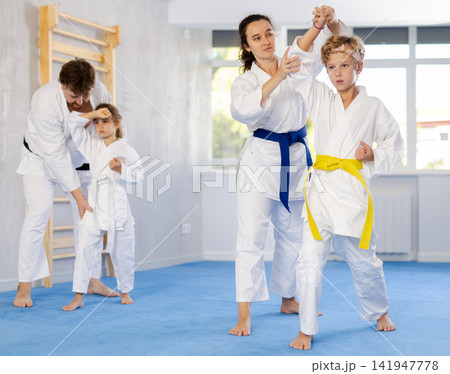 Preteen children performing kata exercises under guidance of parents Preteen children performing kata exercises under guidance of parents 141947778