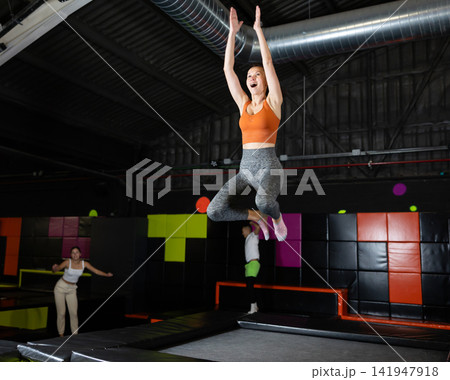 Happy middle aged woman practicing and jumping on trampolines in a sports indoor center, workout and modern entertainment concept Happy middle aged woman practicing and jumping on trampolines in a sports indoor center, workout and modern entertainment concept 141947918