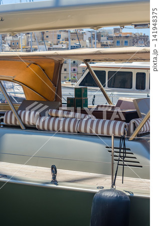 Elegant yacht deck featuring striped lounge cushions, tan canvas bimini tops, and a scenic view of a historic Mediterranean harbor town. High quality photo 141948375