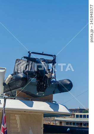 Close-up of a rigid inflatable tender boat with black outboard engine mounted on top of a superyacht, with British flag and harbor view. . High quality photo Close-up of a rigid inflatable tender boat with black outboard engine mounted on top of a superyacht, with British flag and harbor view. . High quality photo 141948377