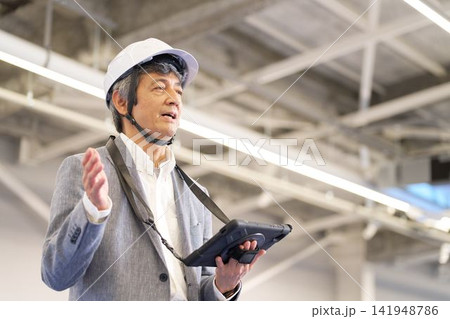 現場でプレゼンをするヘルメット着用のシニア男性 現場でプレゼンをするヘルメット着用のシニア男性 141948786