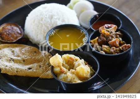 Traditional Indian Bengali vegetarian thali meal platter with rice dal vegetables curry and salad on a black plate Traditional Indian Bengali vegetarian thali meal platter with rice dal vegetables curry and salad on a black plate 141949825