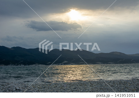 Sunset over a tranquil sea with mountain silhouette Sunset over a tranquil sea with mountain silhouette 141951051