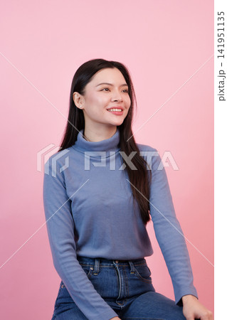 Asian woman smiling in blue turtleneck sweater against pink background Asian woman smiling in blue turtleneck sweater against pink background 141951135