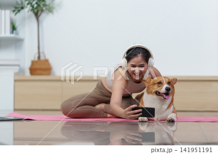 Asian woman taking selfie with Corgi dog on yoga mat at home Asian woman taking selfie with Corgi dog on yoga mat at home 141951191