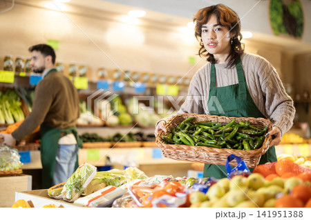 Young female seller holding basket of green long peppers in grocery market 141951388