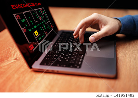 Hands using a laptop to review an emergency evacuation plan on a computer screen indoors Hands using a laptop to review an emergency evacuation plan on a computer screen indoors 141951492