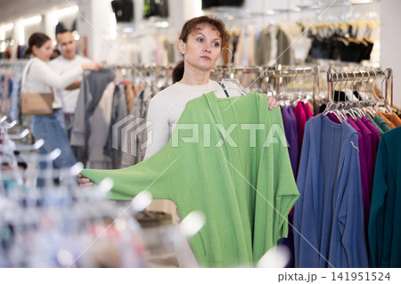 Adult woman chooses cardigan in store Adult woman chooses cardigan in store 141951524