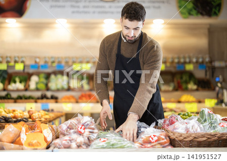Young male seller putting long green peppers on counter in grocery market 141951527