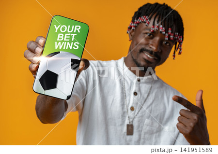 Man smiles and shows phone with winning sports bet in bright setting Man smiles and shows phone with winning sports bet in bright setting 141951589