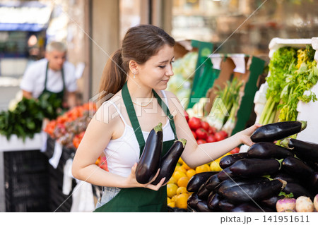 Woman seller carefully arranges eggplants Woman seller carefully arranges eggplants 141951611