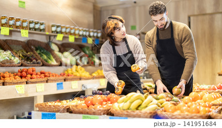 Male and female sellers placing persimmons and mangos on product stand in grocery market Male and female sellers placing persimmons and mangos on product stand in grocery market 141951684