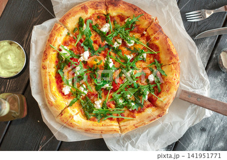 Pizza topped with arugula, cheese, pesto on a wooden table Pizza topped with arugula, cheese, pesto on a wooden table 141951771