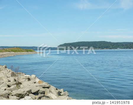 Scenic view of the blue waters of Puget Sound and dense green forest line from a rocky coast. Scenic view of the blue waters of Puget Sound and dense green forest line from a rocky coast. 141951978