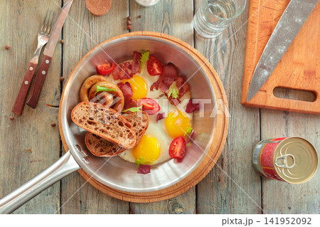 Breakfast plate with eggs, bacon, sausage, and bread on a wooden table 141952092