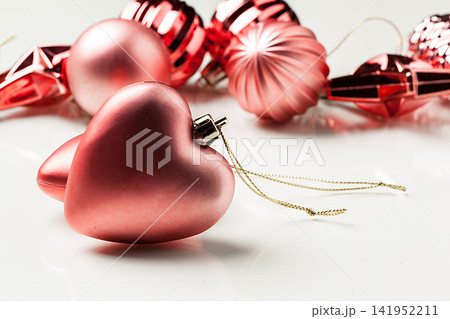 Heart-shaped red ornaments and shiny decorations on a white surface for holiday celebration Heart-shaped red ornaments and shiny decorations on a white surface for holiday celebration 141952211