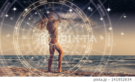 Woman standing on beach with zodiac signs in the sky during sunset Woman standing on beach with zodiac signs in the sky during sunset 141952634