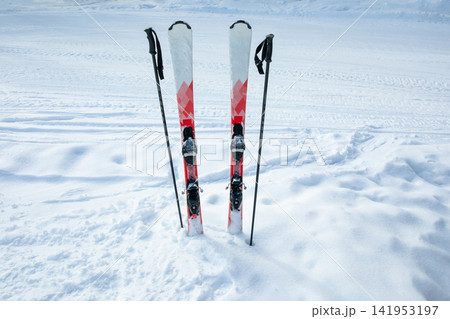 Ski poles and skis stand upright in untouched snow at a ski resort Ski poles and skis stand upright in untouched snow at a ski resort 141953197