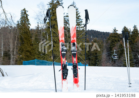 Ski gear positioned upright in snow with mountains in background Ski gear positioned upright in snow with mountains in background 141953198