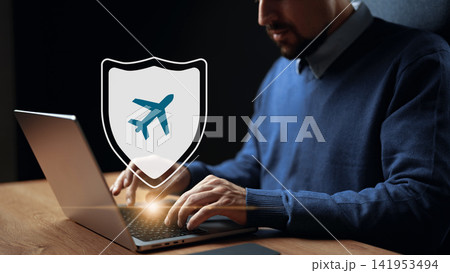Man booking travel online while sitting at a desk with a laptop during evening hours in a home office setting Man booking travel online while sitting at a desk with a laptop during evening hours in a home office setting 141953494