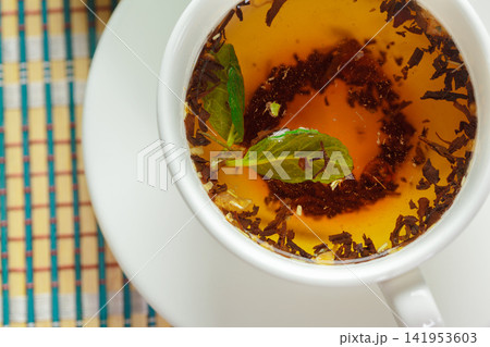 Top view of a cup of brewed tea with fresh Mint leaves on a placemat Top view of a cup of brewed tea with fresh Mint leaves on a placemat 141953603