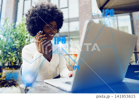 Investor monitors IPO activity while working on laptop at outdoor cafe in urban setting during daytime 141953615
