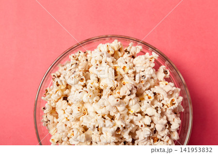 Popcorn in a glass bowl placed on a pink background during a snack time moment Popcorn in a glass bowl placed on a pink background during a snack time moment 141953832