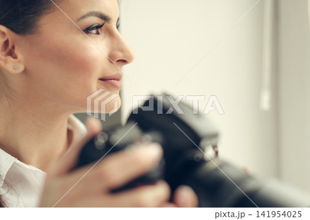 Woman photographer holds camera in studio during daytime shoot Woman photographer holds camera in studio during daytime shoot 141954025