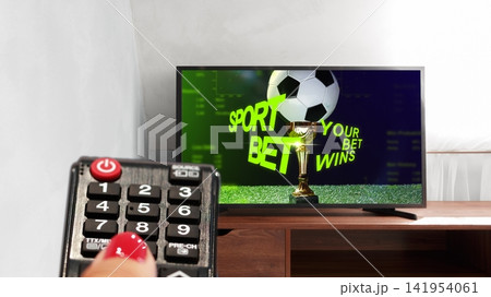 Betting on sports while watching a game on TV at home with a remote control in hand Betting on sports while watching a game on TV at home with a remote control in hand 141954061