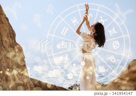 Woman interacts with astrology symbols by the ocean during daylight Woman interacts with astrology symbols by the ocean during daylight 141954147