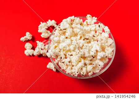 Popcorn sits in a clear bowl on a bright red surface with scattered pieces nearby Popcorn sits in a clear bowl on a bright red surface with scattered pieces nearby 141954246