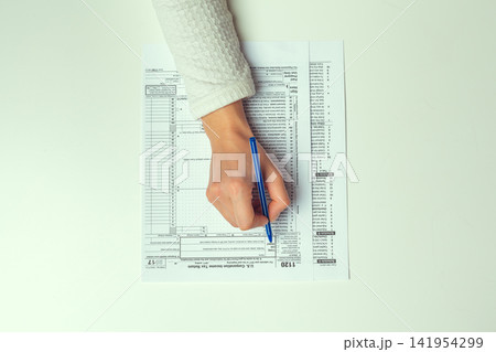 Filling out a U.s. corporation income tax return form 1120 with blue pen Filling out a U.s. corporation income tax return form 1120 with blue pen 141954299