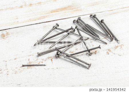 Group of small metal nails on a textured white wood surface Group of small metal nails on a textured white wood surface 141954342