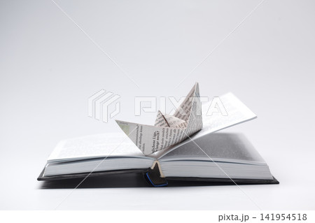 Paper boat sits on open book, pages with writing shown 141954518