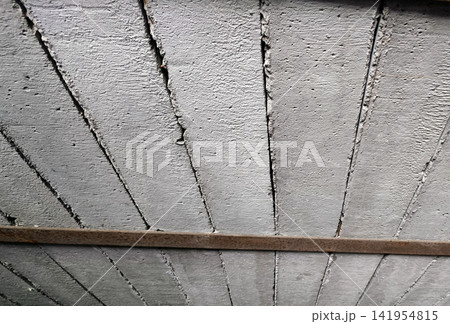 Detailed bottom-up perspective of rough, precast concrete beams forming ceiling structure. Notice the jagged dark seams between slabs, horizontal rusty metal support bar crossing the lower section. 141954815
