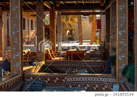 Cafe interior designed in Arabic style, featuring colorful carpets and wooden decor. The space is warm and inviting, with intricate patterns and cozy seating areas. Cafe interior designed in Arabic style, featuring colorful carpets and wooden decor. The space is warm and inviting, with intricate patterns and cozy seating areas. 141955534