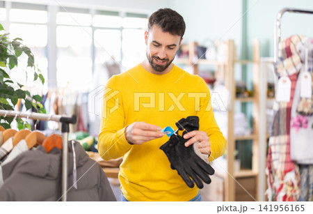 Young man choosing and trying on gloves in clothing store Young man choosing and trying on gloves in clothing store 141956165