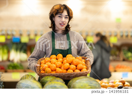 Young woman seller puts tangerines in vegetable shop 141956181
