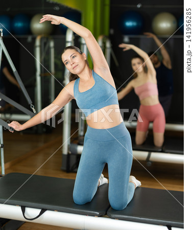Young girl performing pilates reformer stretch during group class 141956285