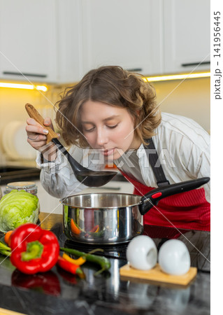 Young woman smelling diet soup while cooking healthy meal in home kitchen with happy satisfied mood 141956445
