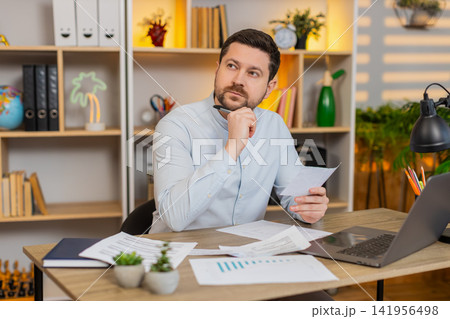 Young man on home table reading contract pages and checking details before signing official letter Young man on home table reading contract pages and checking details before signing official letter 141956498