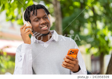 African American young man listening to music walking in city street changing tracks with headphones 141956509