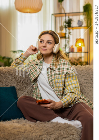 Young woman on home sofa listening to audiobook in headphones and reacting to inspiring thoughts 141956517